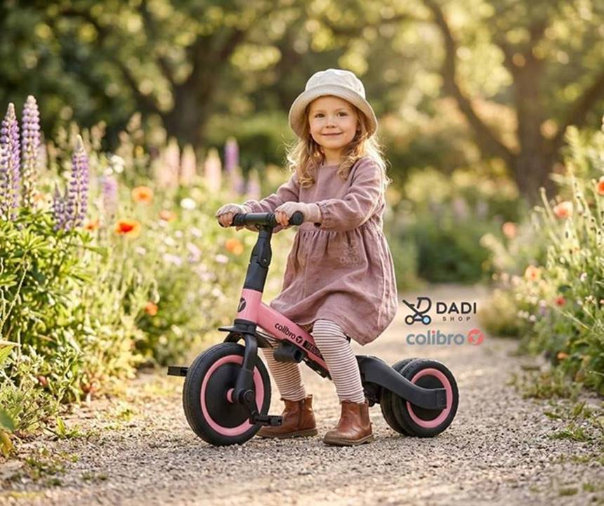 Dziewczynka ok. 3–4 lat na lekkim rowerku biegowym Colibro,ćwiczy równowagę wśród kwitnących łąk.